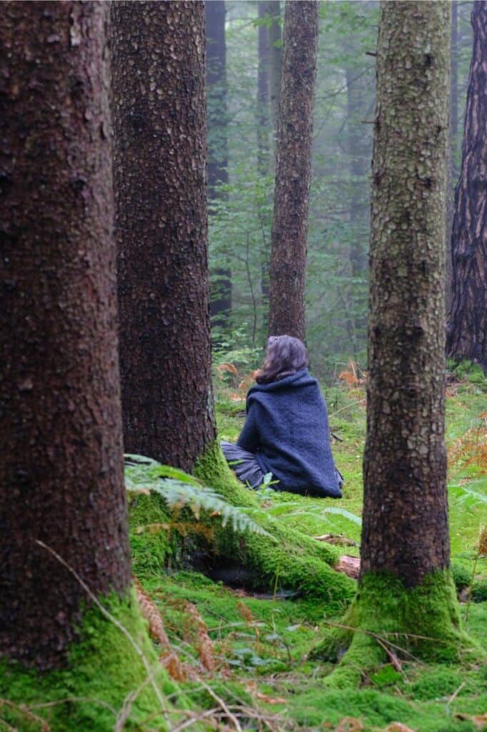Romana Delberg meditiert im Wald des Weltenhofes. Der Waldboden ist moosig und hat jede Menge Farn
