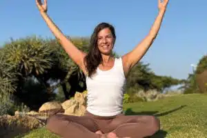 Beate Minkowitsch im Yogasitz mit erhobenen Armen, lächelnd